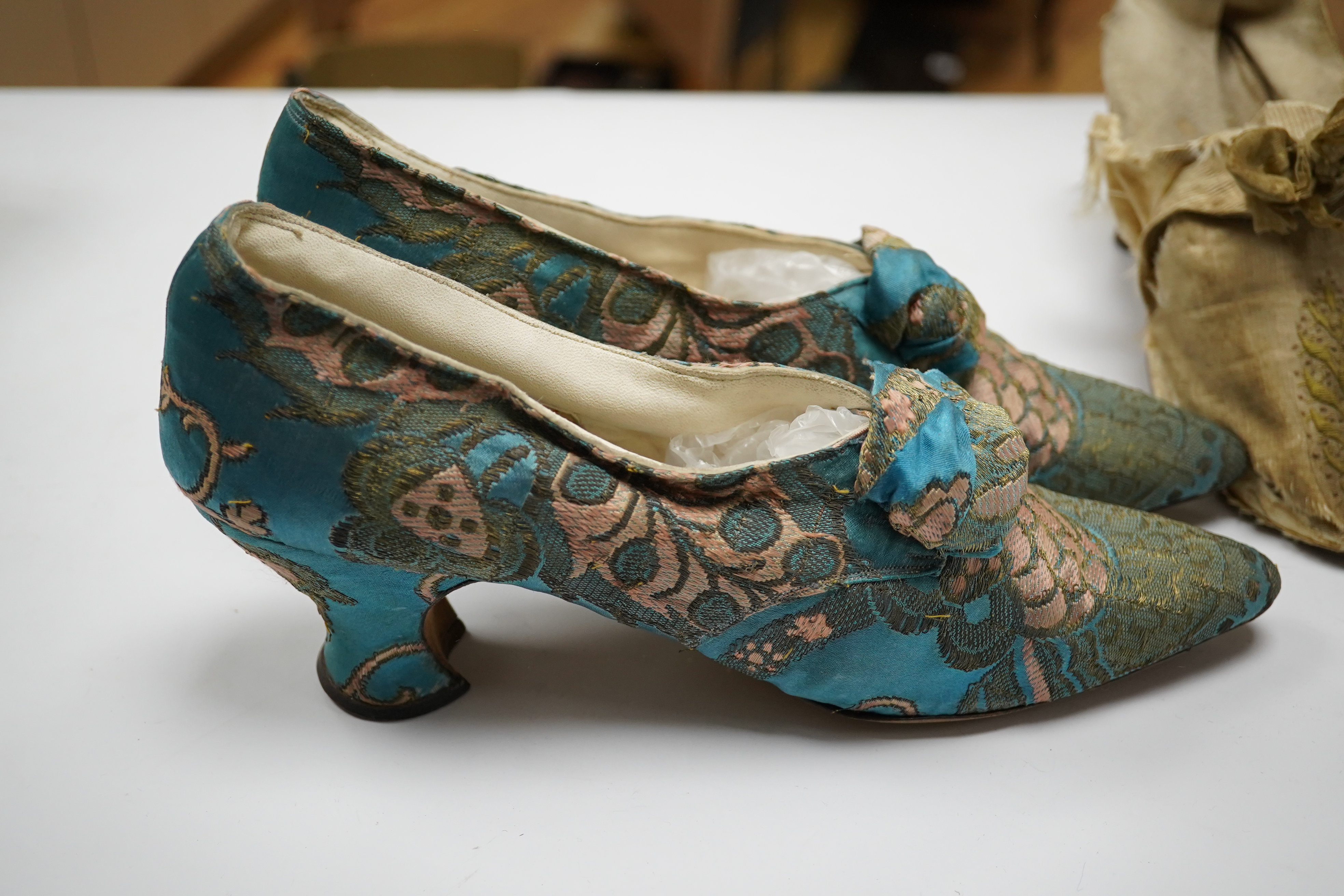 A pair of 18th century cream silk and embroidered ladies shoes together with a later 19th century silk brocade pair of ladies shoes, retailed by C. Moycopf, Burlington Arcade, both pairs lined in soft cream kid leather.